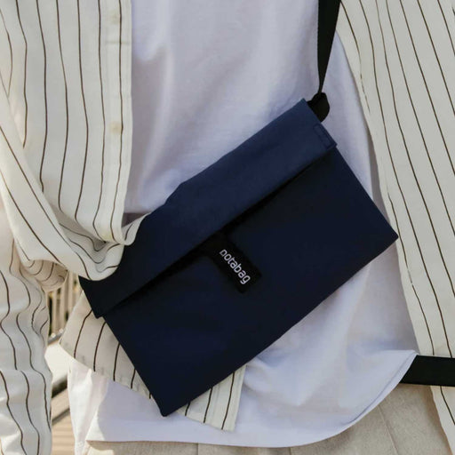 navy notabag with blackopening tab and strap. Worn crossbody over a white tshirt and  white shirt with thin black stripes