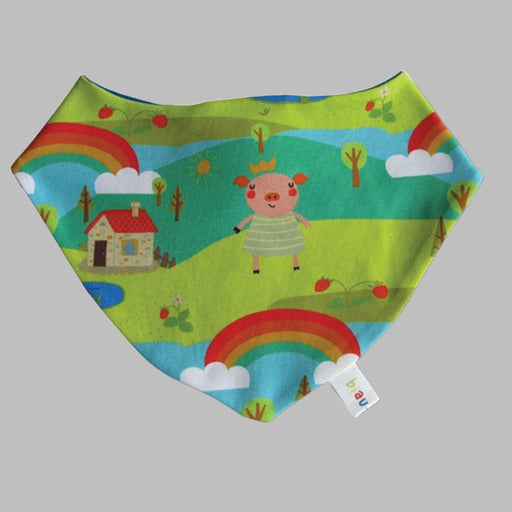 cotton baby dribble bib with pattern of green hill, blue skies , rainbows with smiling pig and house