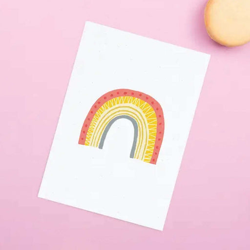 white greeting card with red, yellow and blue rainbow on front against a pink background
