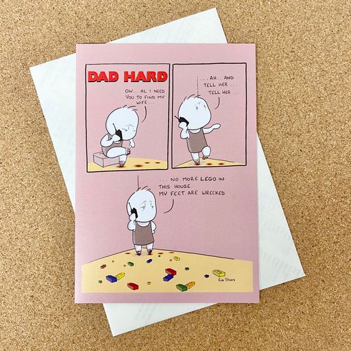 fathers day card with white envelope on cork background. pink card with comic style boxes and image of cartoon dad standing on multicolor lego. 
