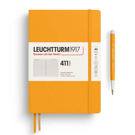 A5 411 YELLOW LEUCHTTURM NOTEBOOK WITH WHITE BANNER WRAP, YELLOW ELASTIC, TWO RIBBON PAGE MARKERS AND GREEN PEN TO RIGHT OF NOTEBOOK