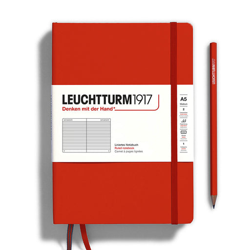 fox red a5 leuchtturm notebook with red elsatic band two red page ribbons, white paper band across cover and red pencil to the right