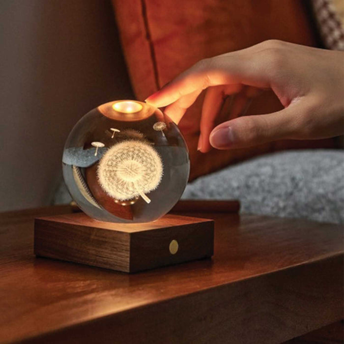 hand touching a glass orb with floating lasersut dandelion inside on a wooden square base