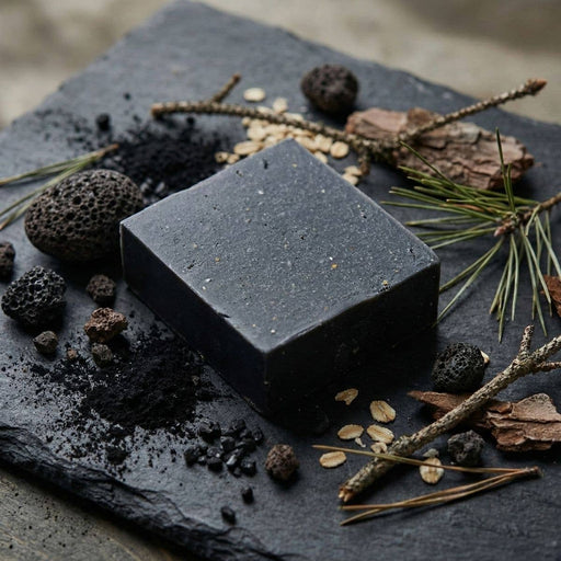 Black soap bar on a dark stone surface with natural elements
