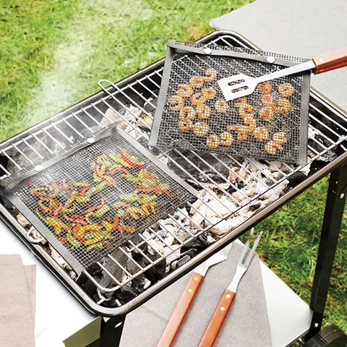 smoking bbq on grass with 2 black mesh bags on it. One with prawns inside, being lifted by bbq tongs and another to left with strips of yellow, green and red peppers inside