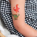 Colorful dinosaur tattoos on a person's arm with a checkered fabric background.