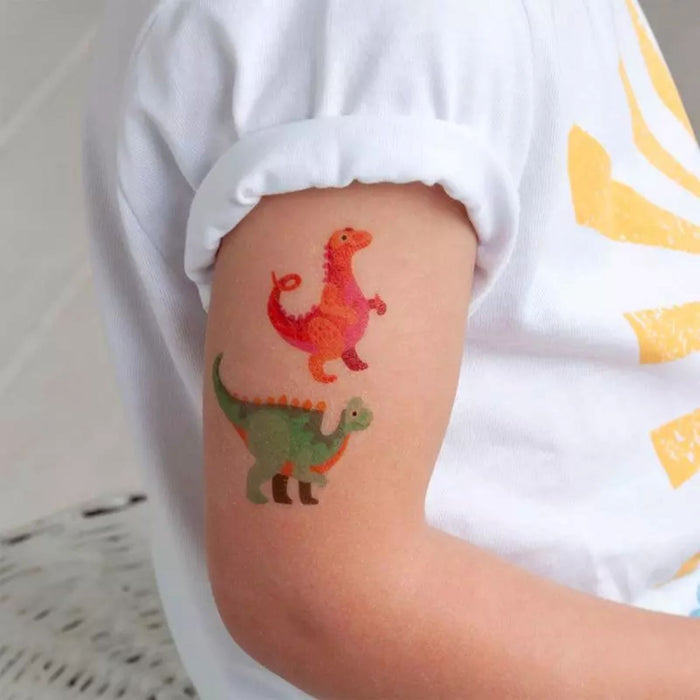Colorful dinosaur tattoos on a child's arm with a white shirt.
