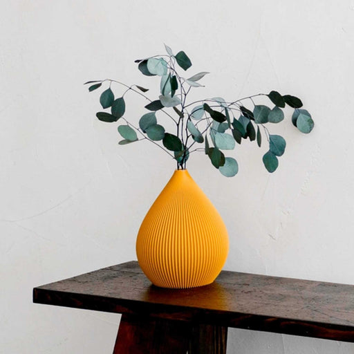 orange ridged teardrop shaped vase with green foliage on a wooden beanch