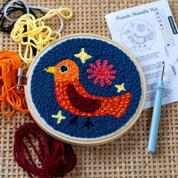 Colourful thread bird punch needle kit in a wooden hoop ring with loose thread around the exterior and a needle with blue handle grip to the right along with instruction leaflet