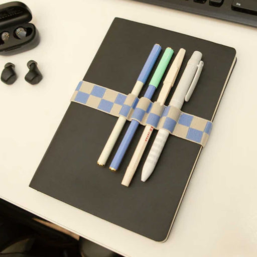 blue and grey checkered elastic book band on a grey notebook, book band is holding 4 pens
