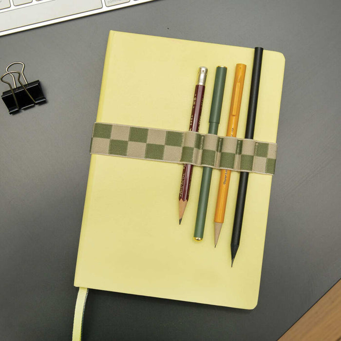 pale yellow notebook with four pens held to it by a green squared book band pen holder