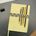 pale yellow notebook with four pens held to it by a green squared book band pen holder