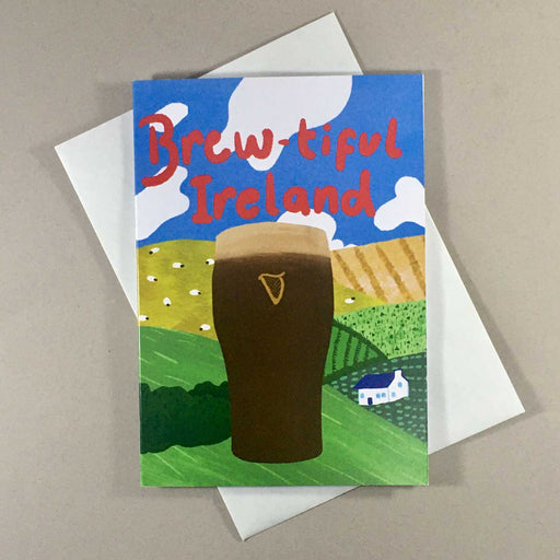 Greeting card with white envelope Card shows a pint of guinness in front of hills and fields with sheep and a blue sky with white clouds
