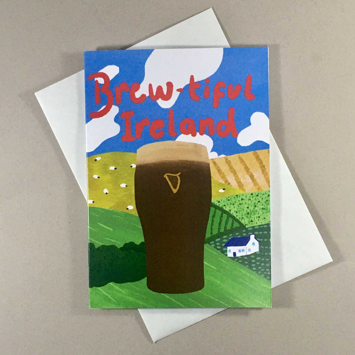 Greeting card with white envelope Card shows a pint of guinness in front of hills and fields with sheep and a blue sky with white clouds
