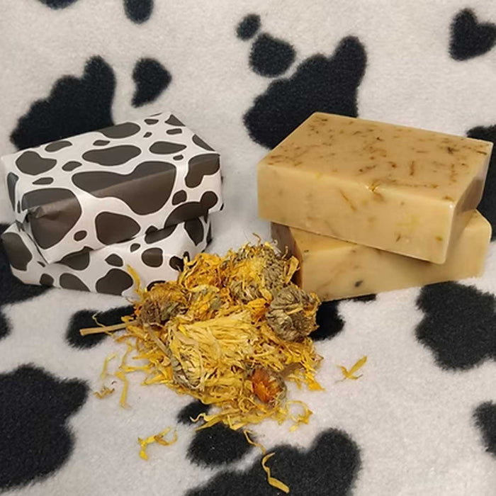 stack of 2 soaps in cow print wrap beside a stack of 2 unwrapped soaps with small pile of dried yellow flowers