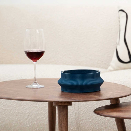 blue ridged bowl on a round wooden table with glass of red wine to the left
