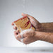 Hand holding a bar of soap with water droplets on a light gray background