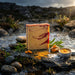 Bar of soap with red swirls on a rock by a body of water, surrounded by nature.