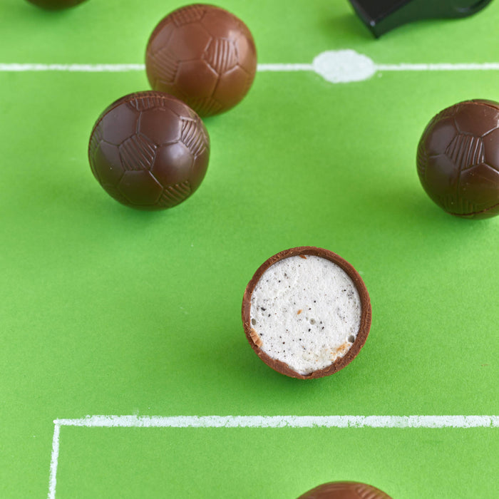 Chocolate soccer balls on a green surface resembling a soccer field with a whistle.