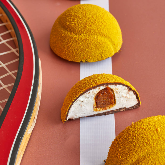 Yellow textured chocolate marshmallow tennis ball dessert on a pink background