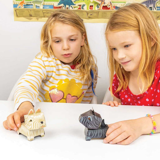 two blond haired children sitting at a white table each holding a small cardboard dog, one white dog, one black dog