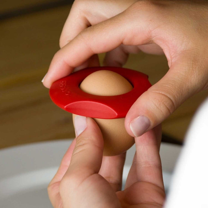 hands holding onto the top of a egg a a red plastic circular tool with hold in centre 