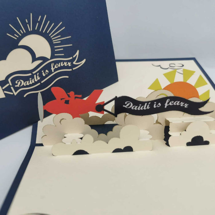 ard":

laser cut Pop-up Father's Day card featuring an airplane and  banner with 'Daidí is Fearr' (Irish for 'Daddy is the Best'). the airplane is flying above clouds and the sun is behind it