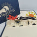ard":

laser cut Pop-up Father's Day card featuring an airplane and  banner with 'Daidí is Fearr' (Irish for 'Daddy is the Best'). the airplane is flying above clouds and the sun is behind it