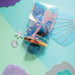 iridescent pocket case with pair of blue sunglasses inside on a blue backdrop with paper shells and starfish i