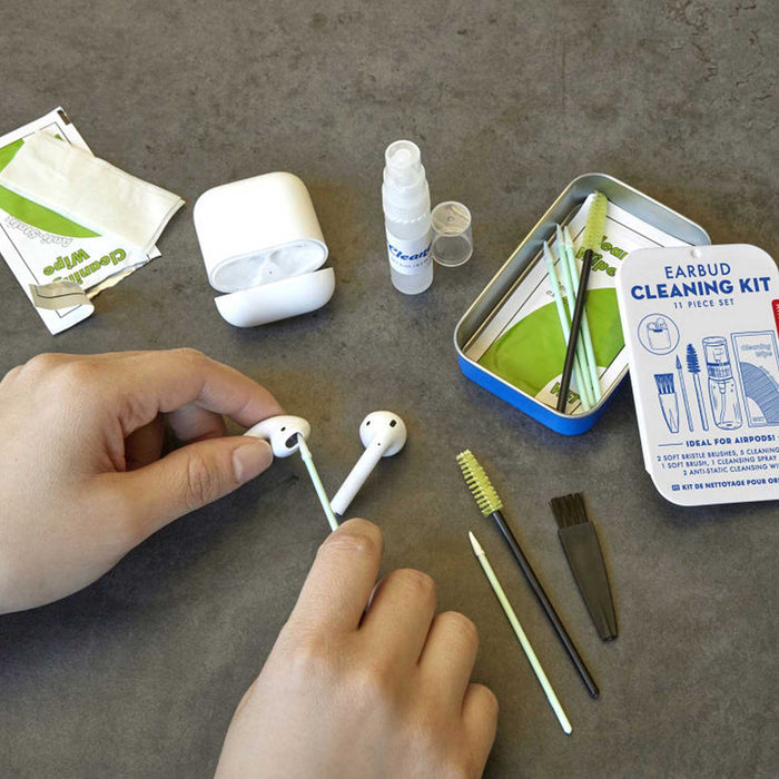 hands cleaning a pair of white earphones with a cleaning bud. Earbud Cleaning Kit tin is to the right