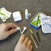 hands cleaning a pair of white earphones with a cleaning bud. Earbud Cleaning Kit tin is to the right