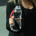 woman dressed in black holding out a clear water bottle with a red Black and Blum tag attached to a metal loop on the mouth of the bottle