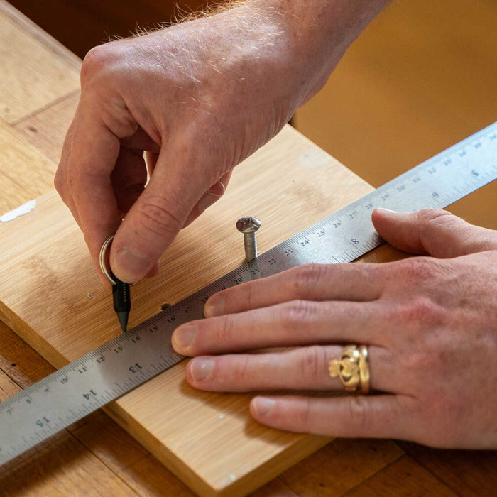 Stainless steel Everlasting Pencil Keychain with built-in graphite pencil and flathead screwdriver, compact size, being used to make a mark on a bit timber