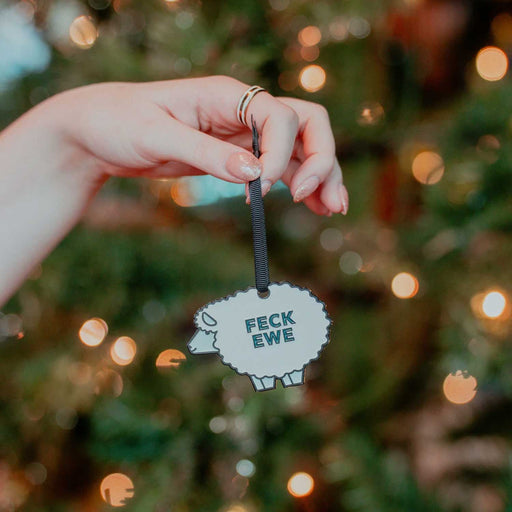 hand hold a sheep xmas tree decoration on a black ribbon with feck ewe written on sheeps body