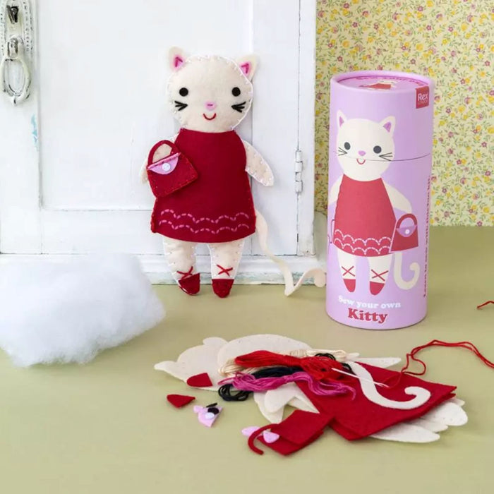 Plush cat toy with a dress and accessories next to a cylindrical packaging labeled 'Kitty'.