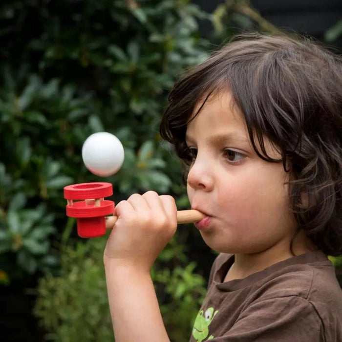 Child blowing a ball with a wooden pipe outdoors