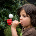 Child blowing a ball with a wooden pipe outdoors