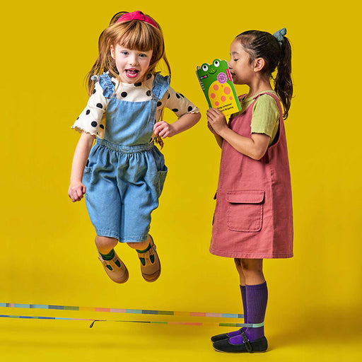 two children against a yellow background, playing with a skipping rope. One is jumping and the other is holding  green book