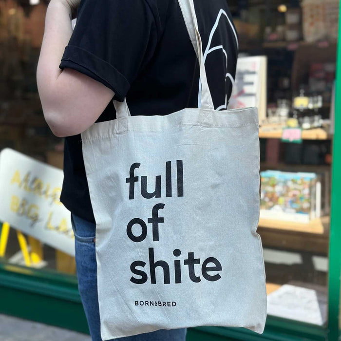 white canvas tote bag on a persons shoulder, with full of shite writen on the tote bag in black lowercase text