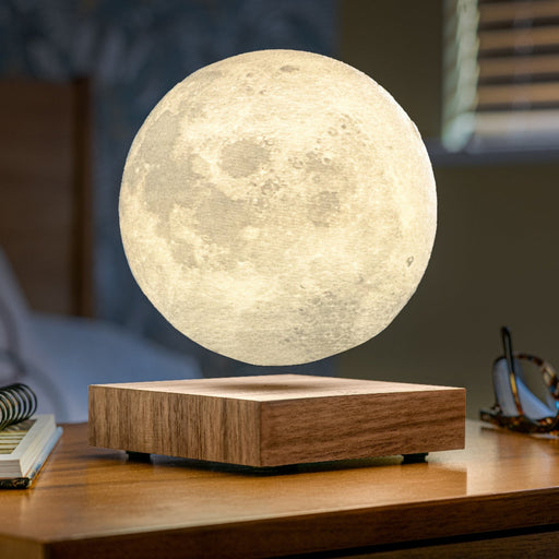 Levitating moon lamp on a wooden base with books and glasses in the background