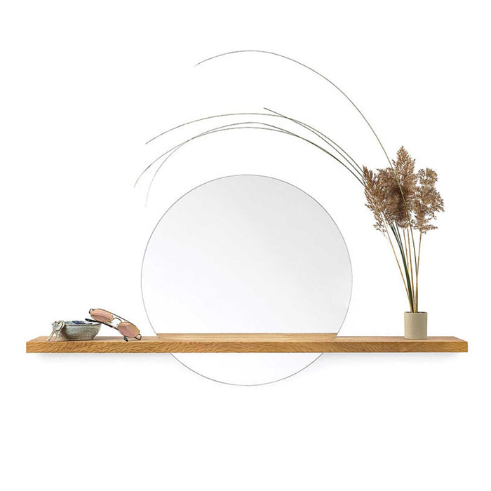round mirror with wooden shelf sitting in front. on the shelf there in a vase of foliage and grasses and to the left a pair of glasses and a bowl with keys