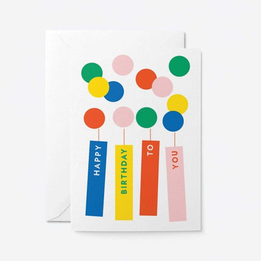 WHITE GREETING CARD WITH 4 COLOURED CANDLES WITH HAPPY BIRTHDAY TO YOU WRITTEN ON THEM AND TWELVE COLOURED CIRCLES ABOVE RESPRESENTING FLAMES