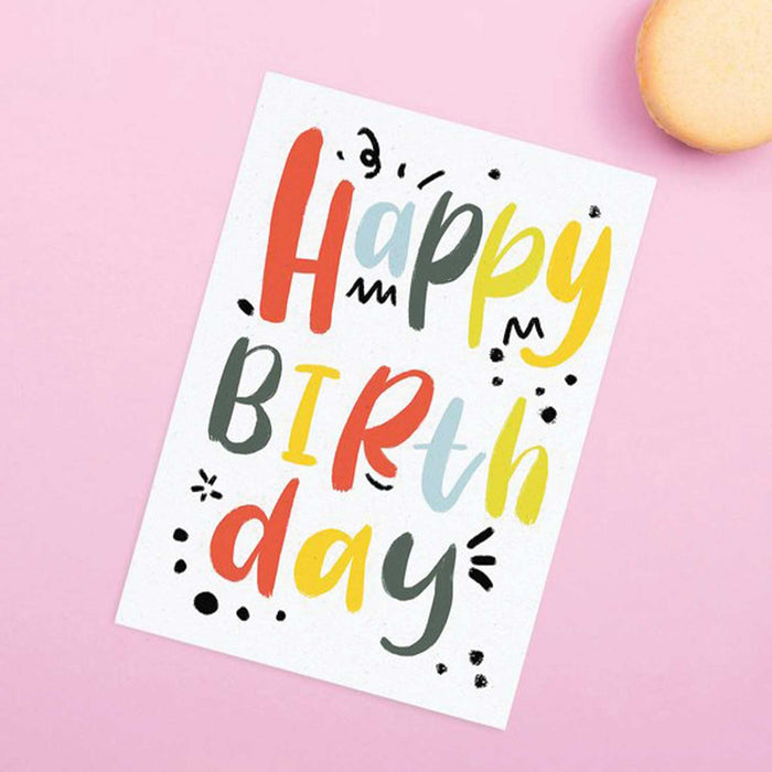 white textured card with Happy Birthday in bright multi coloured text on front on pink background