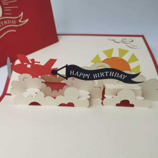 open pop up card with sun red plane clouds and happy birthday banner
