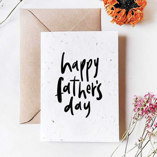 white card with Happy Father's Day in black text on a white greeting card with brown envelop behind and a n orange flower in top right corner