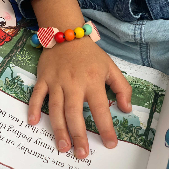 CHILDS HEAND WEARING A WOODEN BEAD BRACELET WITH TWO RED STRIPY HEART BEADS
