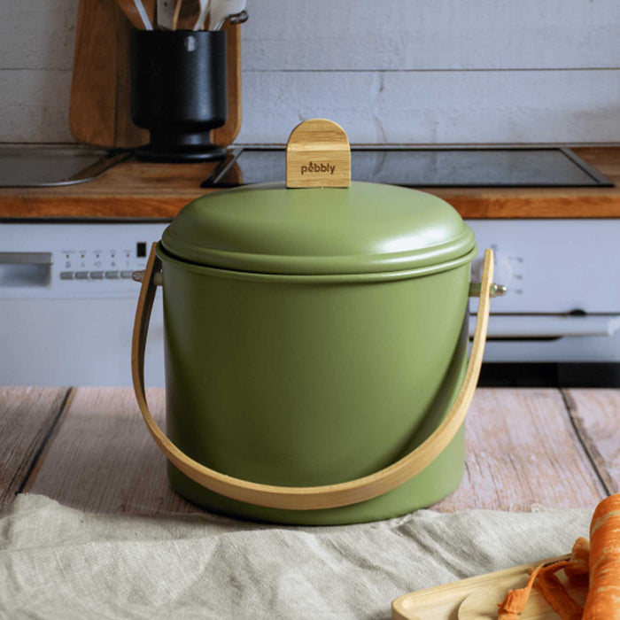 small green metal bin with matching lid and bamboo handle sitting atop a kitchen counter