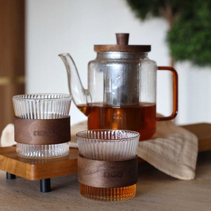 Karl Tea Set with clear glass teapot and two glasses. both have ridged bodies and amber brown handles. the two glasses have a wooden band around the centre and the teapot ahas a wooden lid