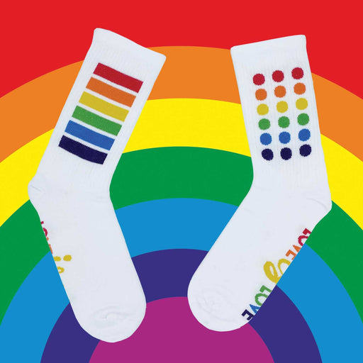 pair of white socks, sock on right has rainbow coloured dots, while sock on left has 6 rainbow coloured strips. Socks are in front of a rainbow background