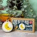 Cross stitch mini kit with 'Love You to the Moon & Back' design on a wooden surface with plants in the background.